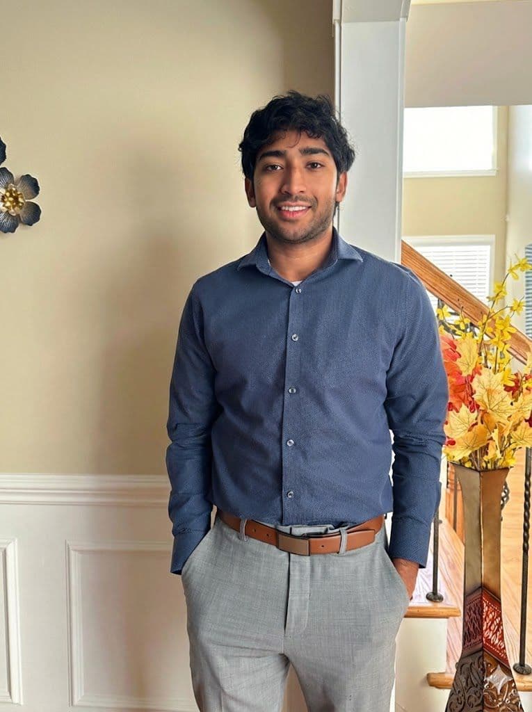 Saiesh Malluri smiling in a dark blue patterned shirt and grey trousers, hands in pockets, indoors — Knoxville Telugu Association leadership